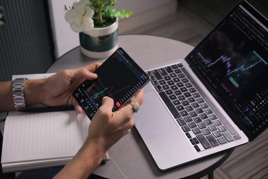 Hands typing on a laptop with cryptocurrency charts and smartphone display in view, focusing on digital finance.